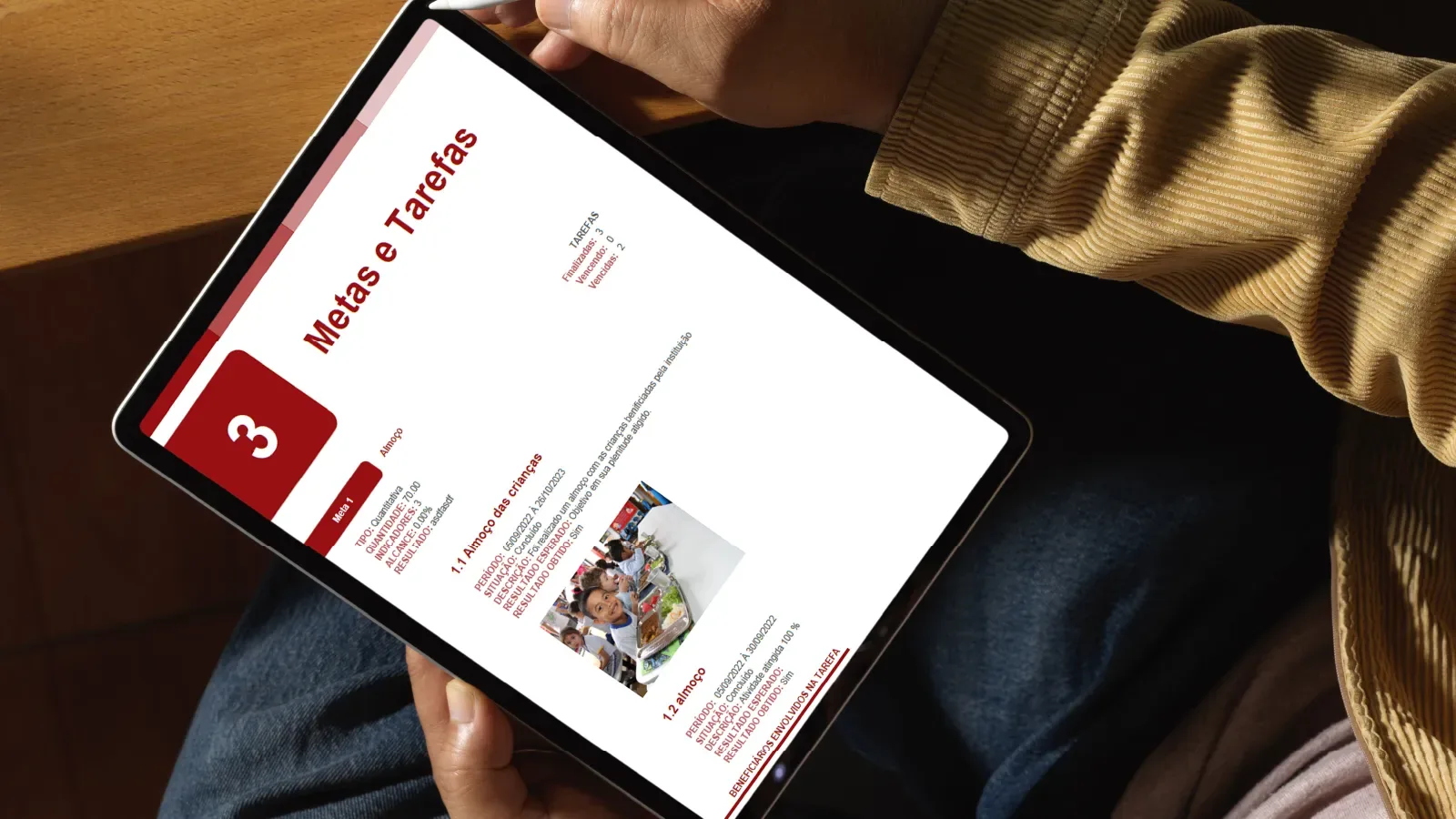 Pessoa segurando um tablet que exibe a tela de metas e tarefas de um projeto