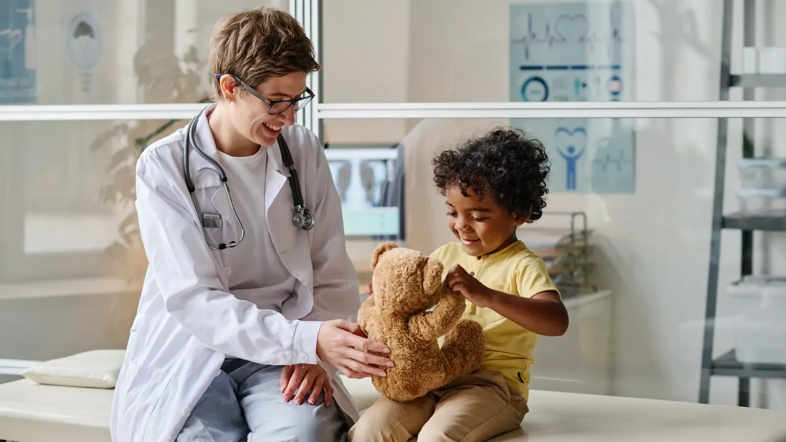 Profissional de saúde em atendimento a uma criança, que segura um urso de pelúcia