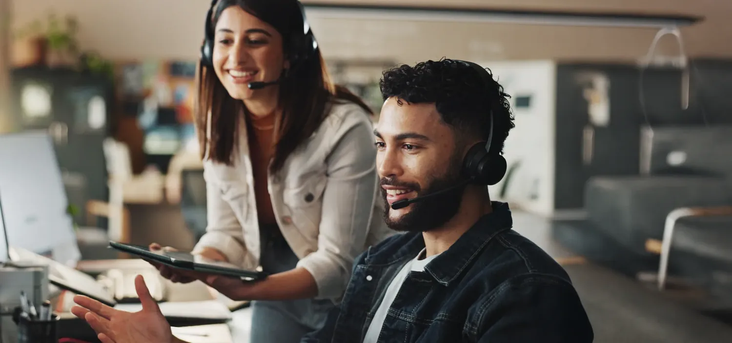 Duas pessoas de uma equipe de atendimento diante do computador, uma delas com fone de ouvido