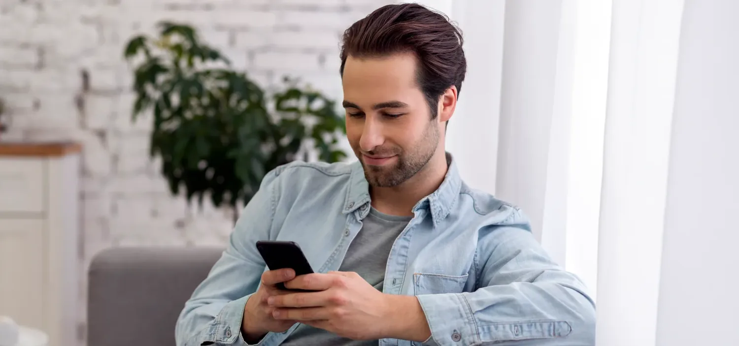 Homem sentado consultando o celular em ambiente claro
