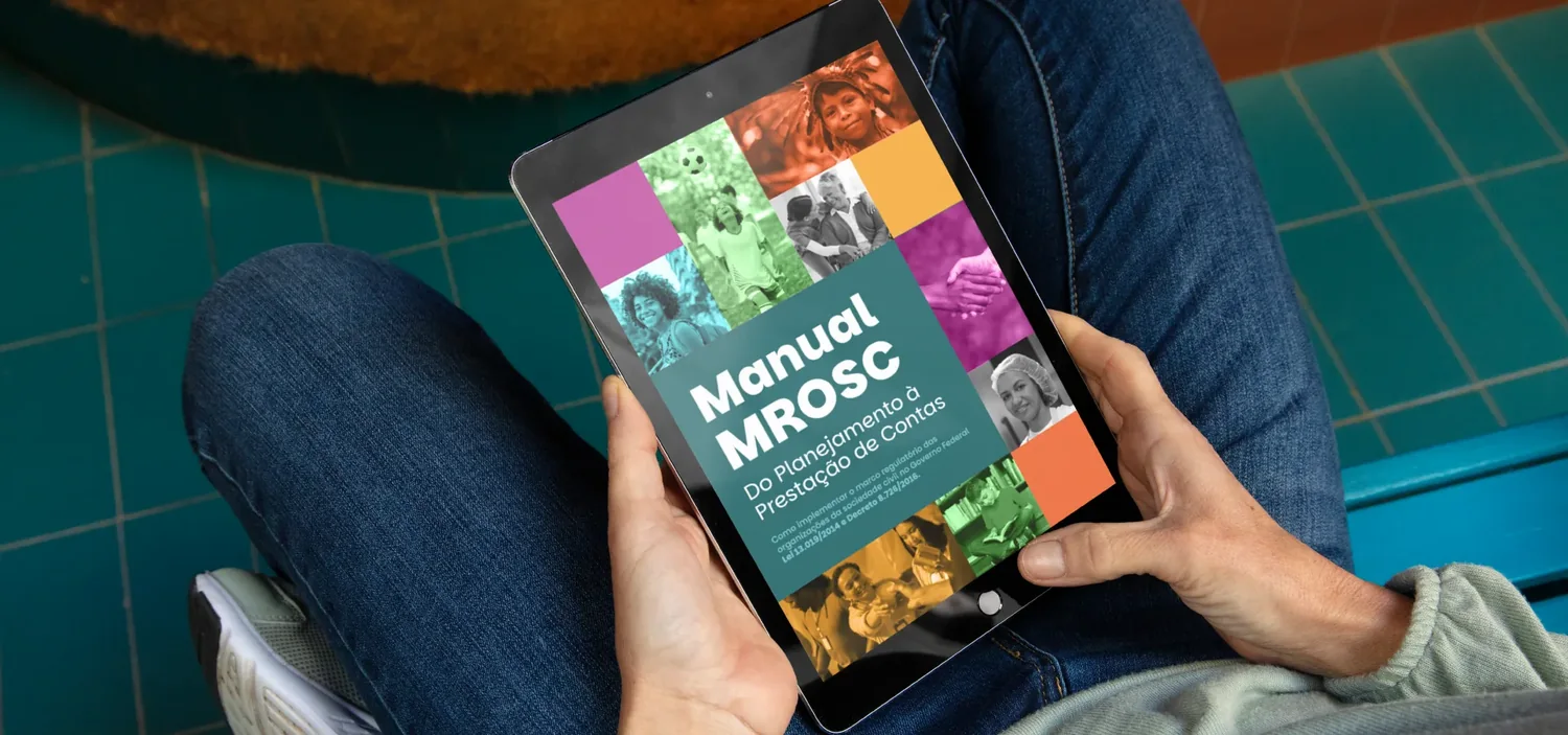 Pessoa sentada segurando um tablet que exibe a capa do Manual MROSC