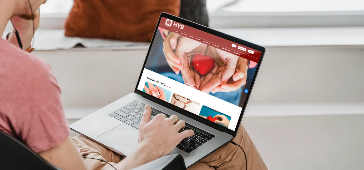 Notebook exibindo o site de uma organiza��o feito no HYB, com a imagem de m�os segurando um cora��o